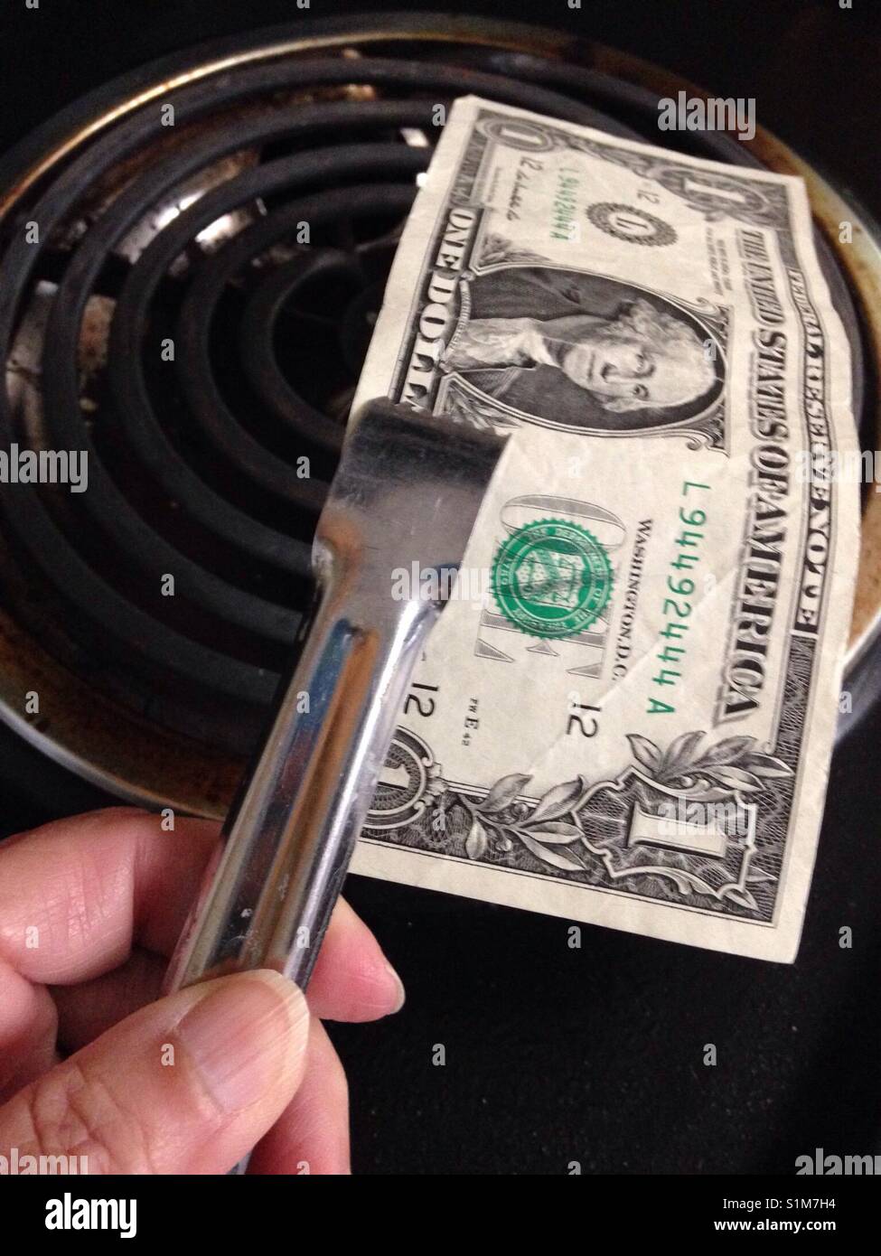 Woman's hand holding tongs holding money over a stove Stock Photo