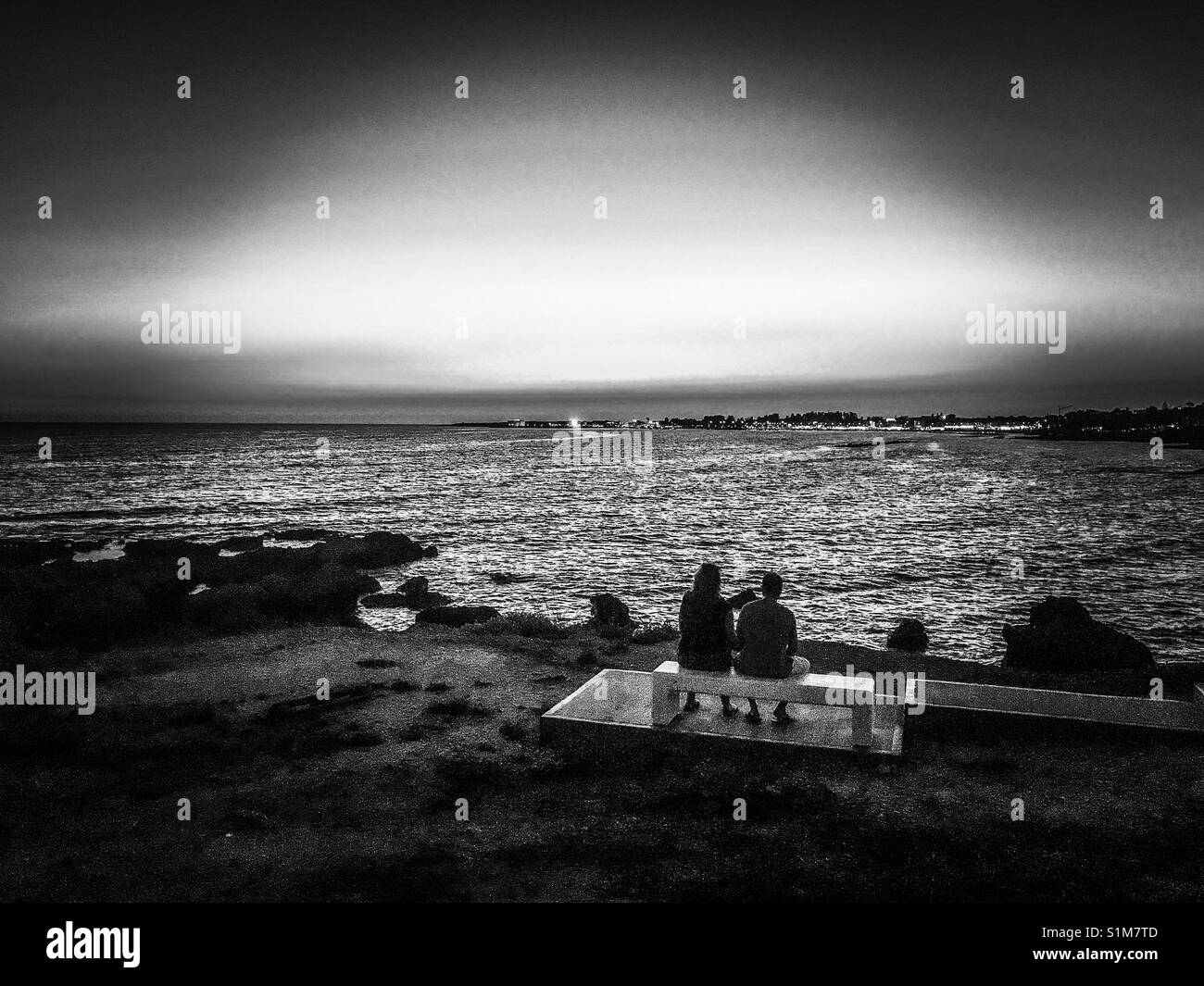 Black and white image of a couple looking at the lights of paphos in the distance - Smartphone Captured Stock Image