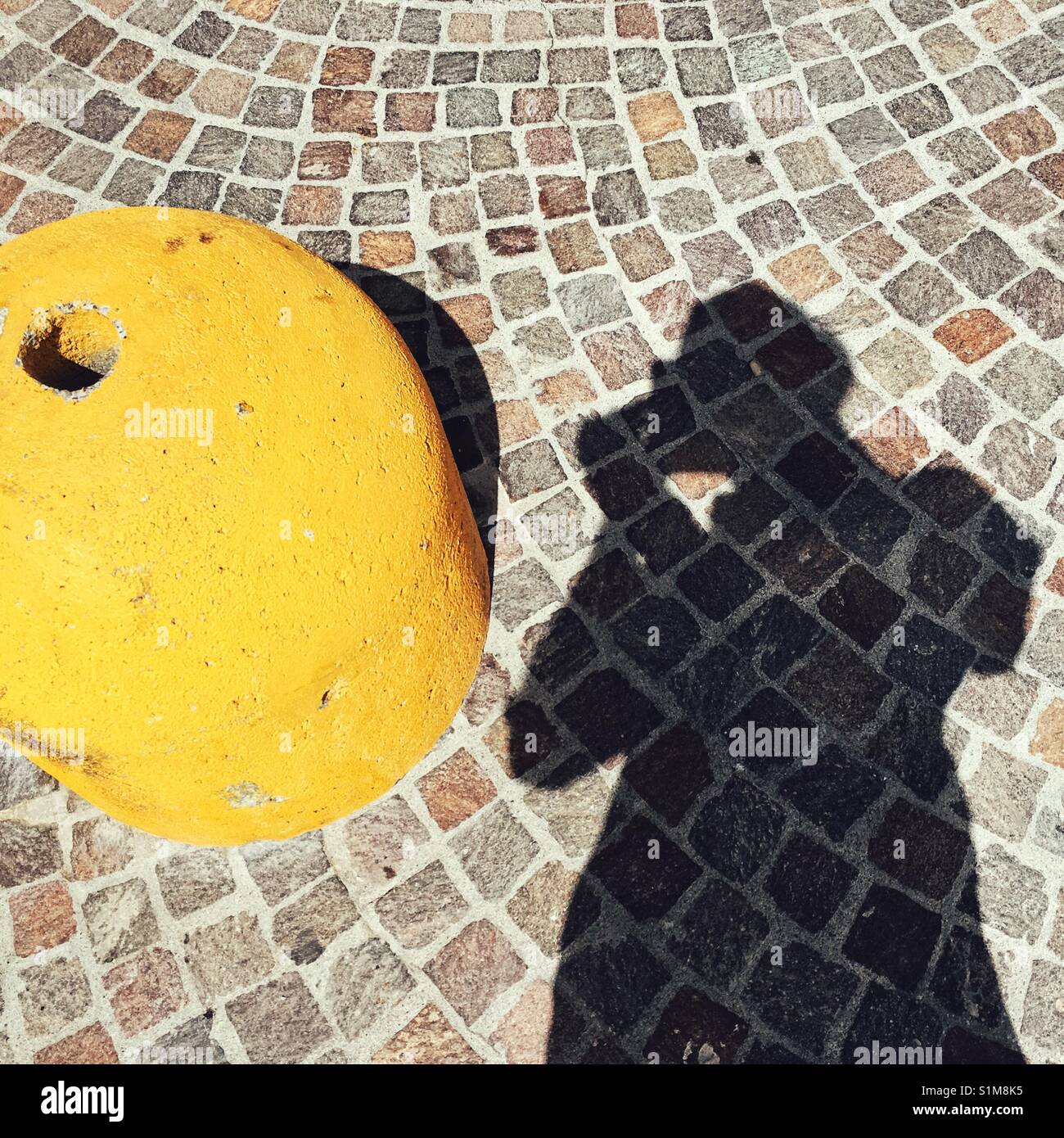 Silhouette of man with camera photographing a yellow bollard - Smartphone Captured Stock Image