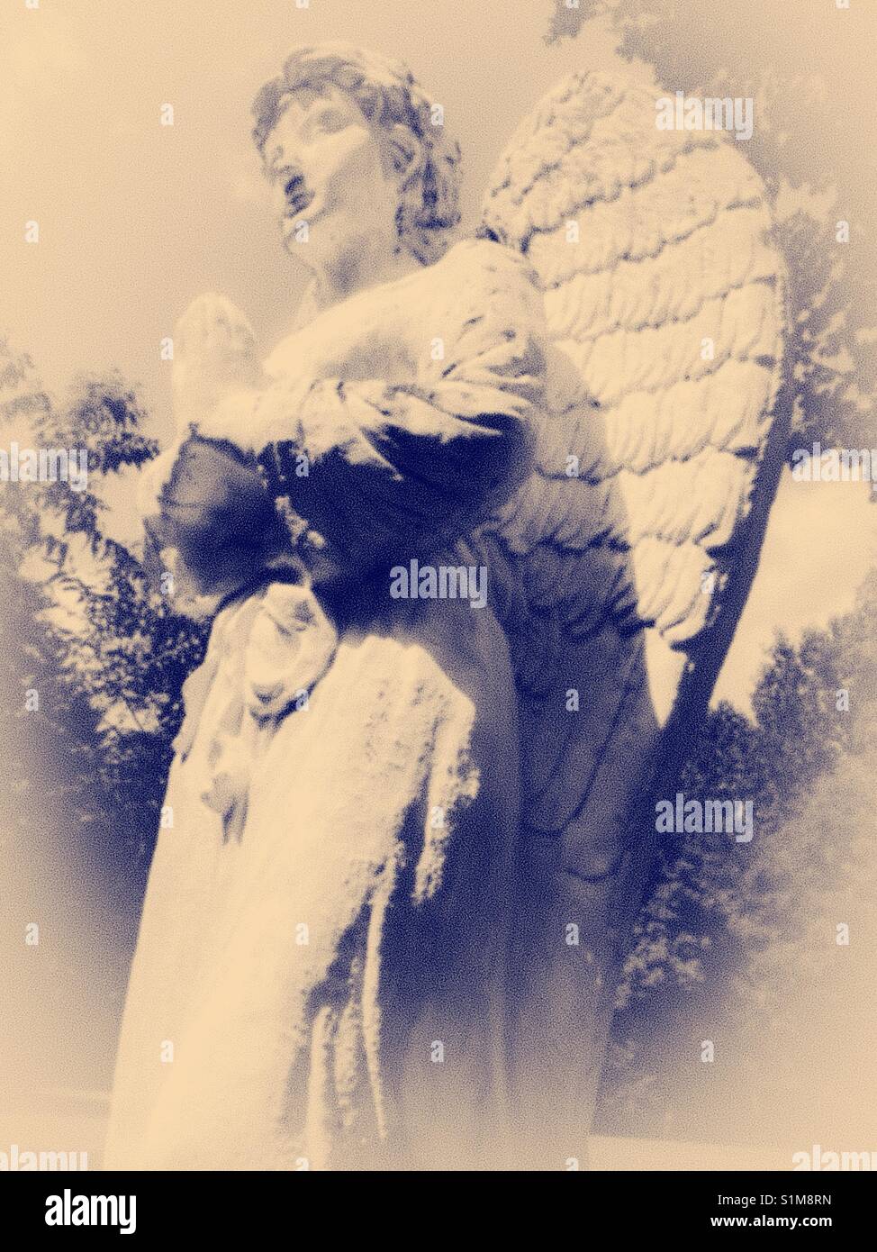 Praying angel- statue of white angel in prayer pose stands in garden Stock Photo