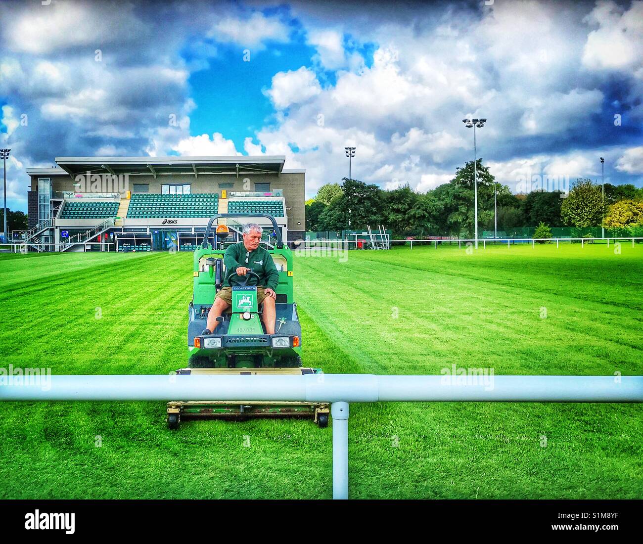 Groundsman cutting the grass of a rugby pitch whilst sitting on the mower - Smartphone Captured Stock Image
