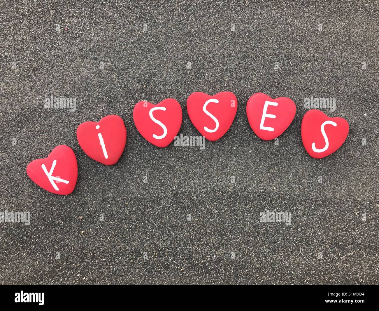 Kissess message with red colored heart stones over black volcanic sand - Smartphone Captured Stock Image