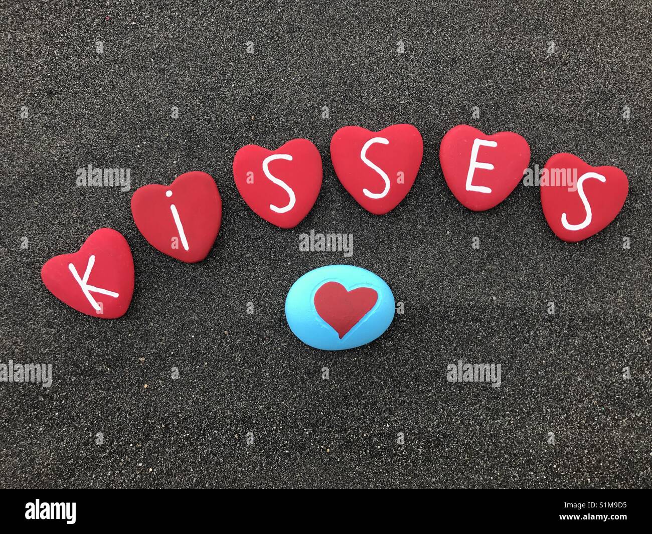 I love you and I send you many kisses with red colored heart stones over black volcanic sand Stock Photo