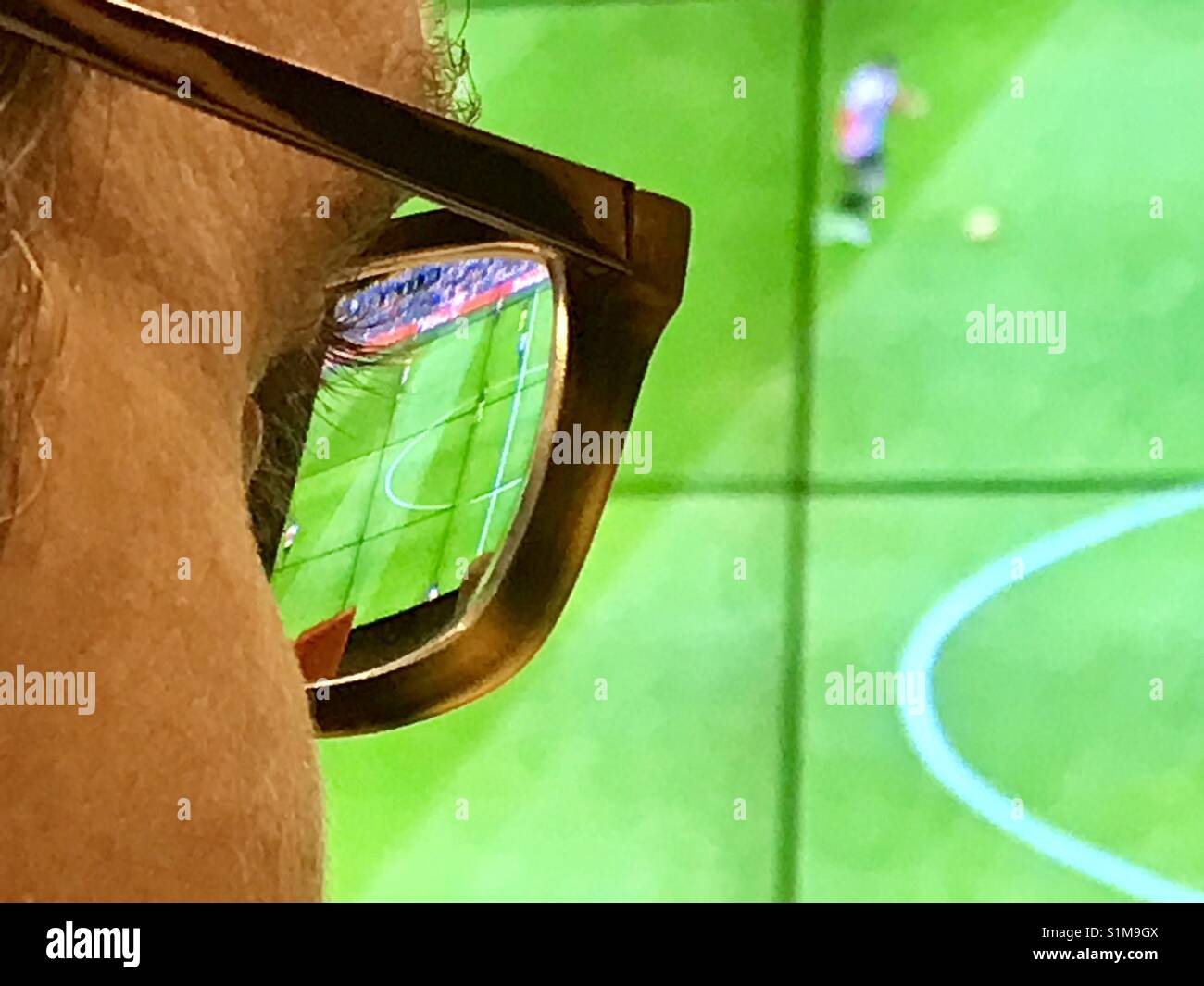 Eyeglasses and eye of a man watching a football match on a big screen. Close view. - Smartphone Captured Stock Image