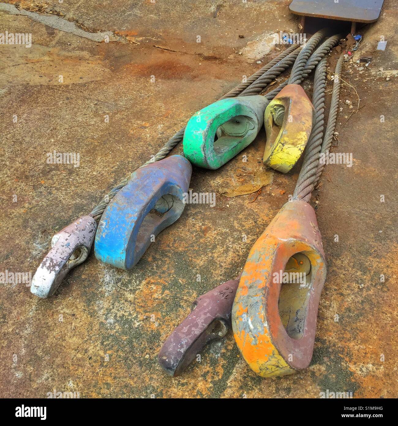 Shipyard ground tackle painted in surprising colors. The ultimate belay anchor; spelter socket terminations on 3-inch-diameter wire rope fastened to deadman anchors. For hauling ships. Stock Photo