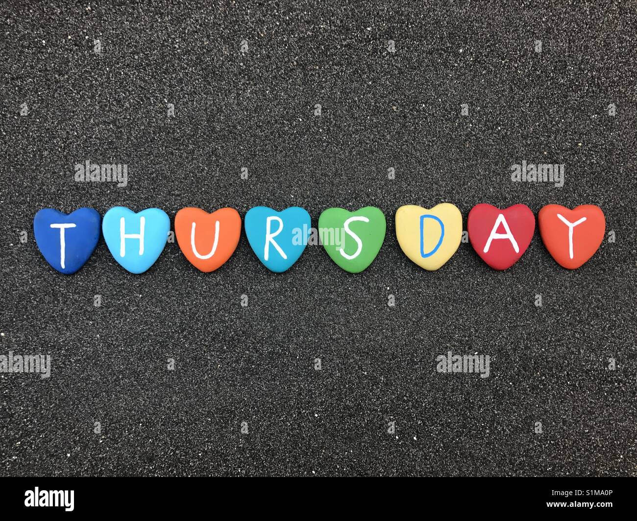 Thursday, day of the week with multicolored heart stones over black volcanic sand - Smartphone Captured Stock Image