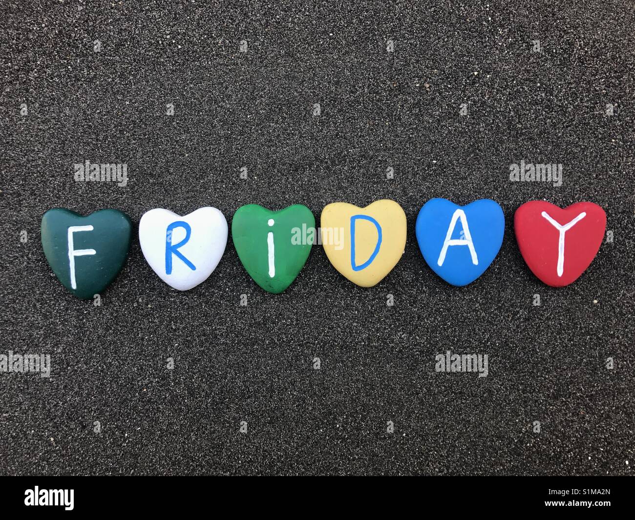 Friday, day of the week with multicolored heart stones over black volcanic sand - Smartphone Captured Stock Image