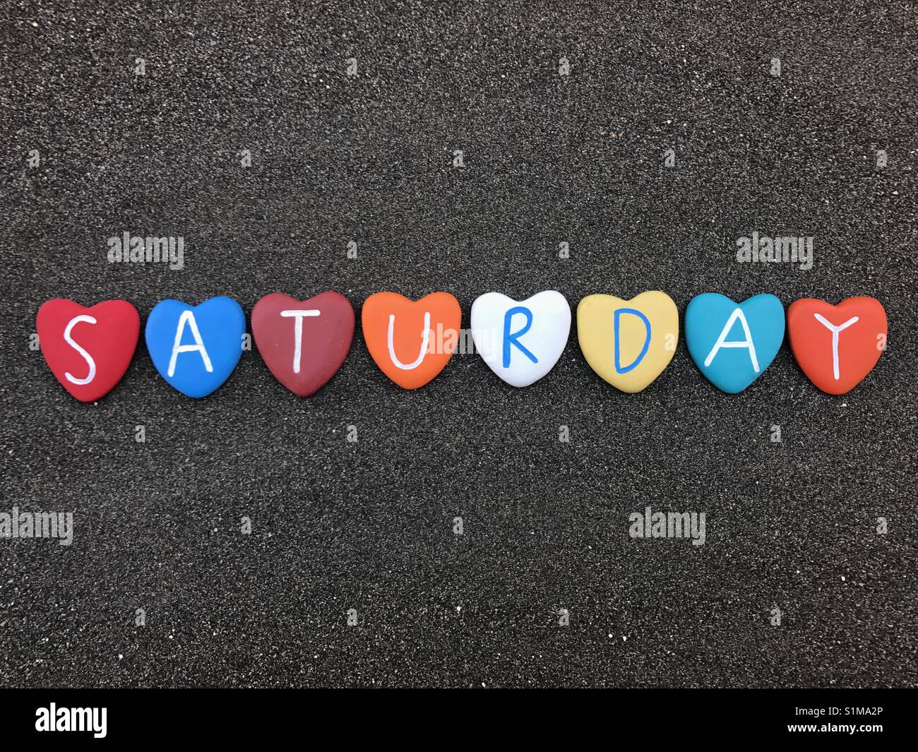 Saturday, day of the week with multicolored heart stones over black volcanic sand - Smartphone Captured Stock Image