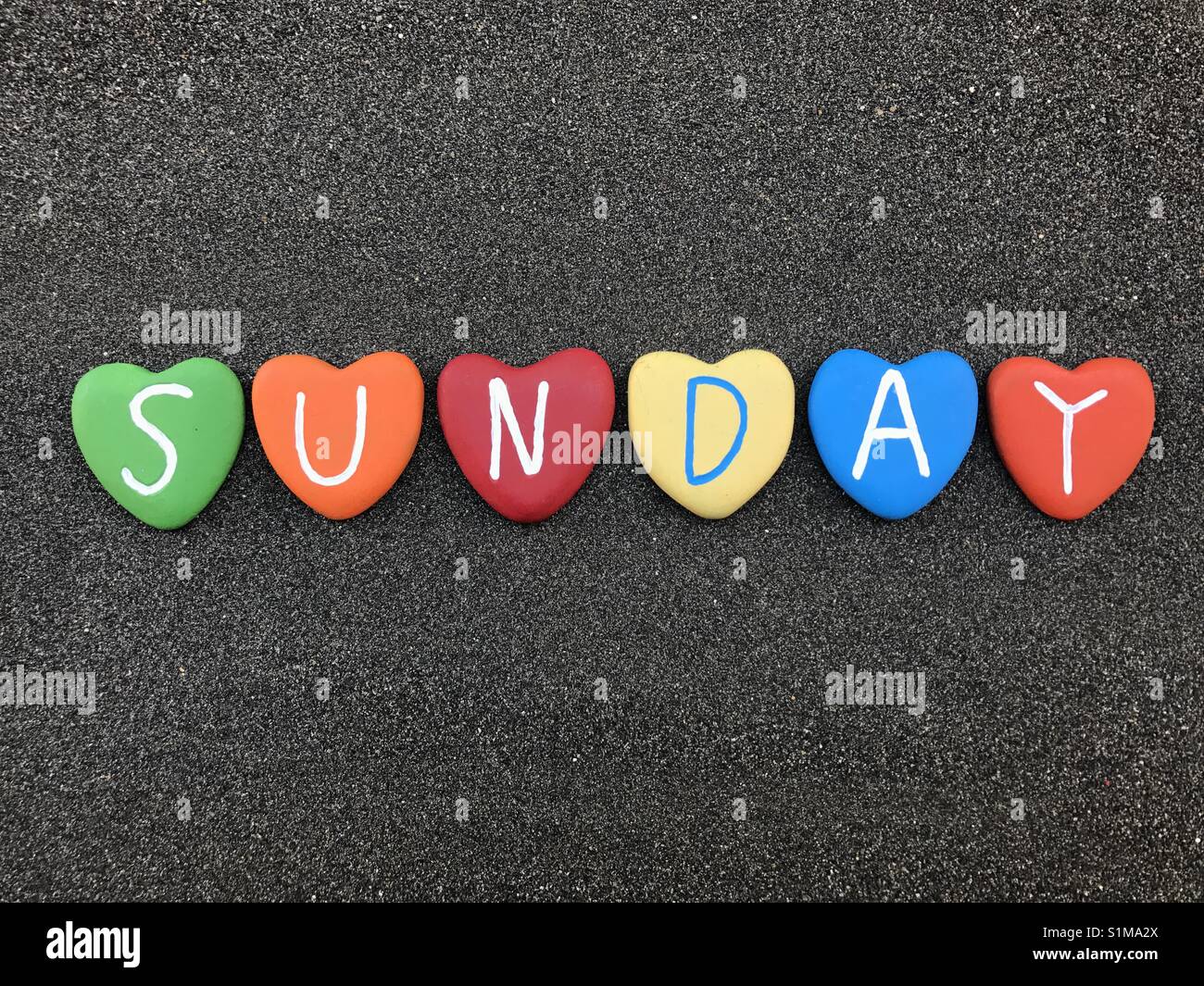 Sunday, day of the week with multicolored heart stones over black volcanic sand - Smartphone Captured Stock Image