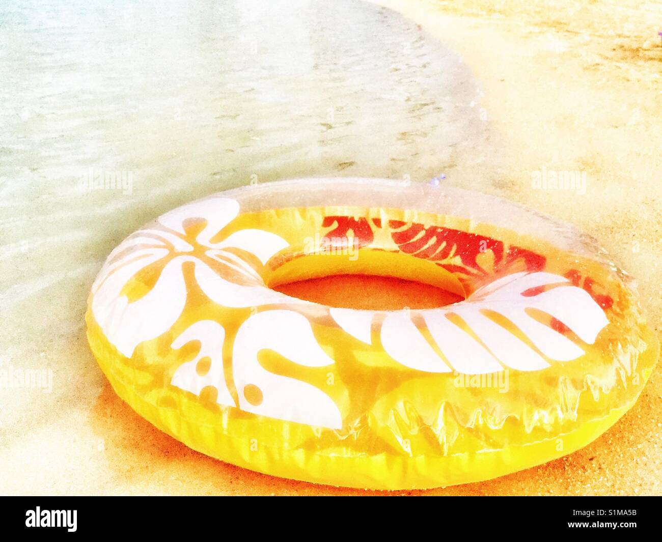 Inflatable ring with orange and tropical pattern at waters edge on beach Stock Photo