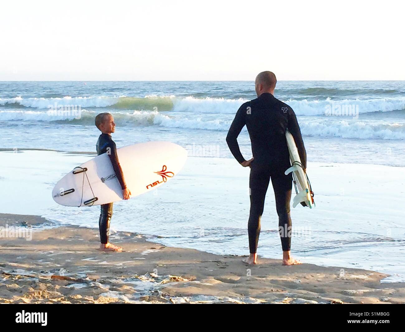 Father and son surfers standing on beach checking out the waves. Pismo Beach, California, United States Stock Photo