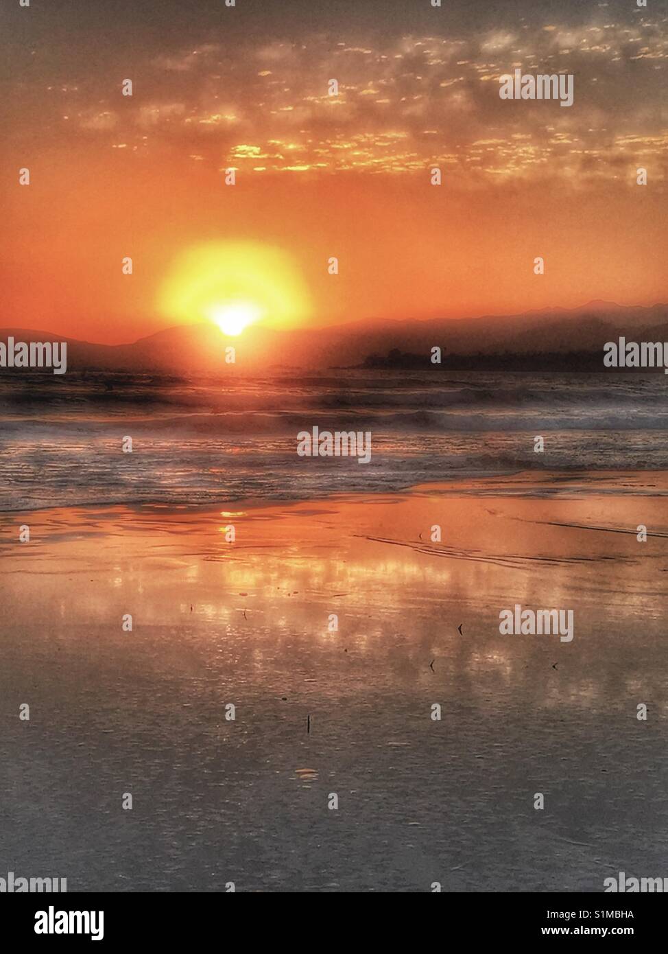 Looking out from the beach at stunning orange sunset over the ocean waves. West coast, California, United States Stock Photo