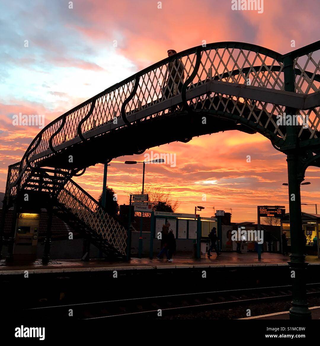 Reforest, Pontypridd, Wales - December 2016: A passenger crosses the railway bridge against the orange glow of dawn on a fine winter's day - Smartphone Captured Stock Image