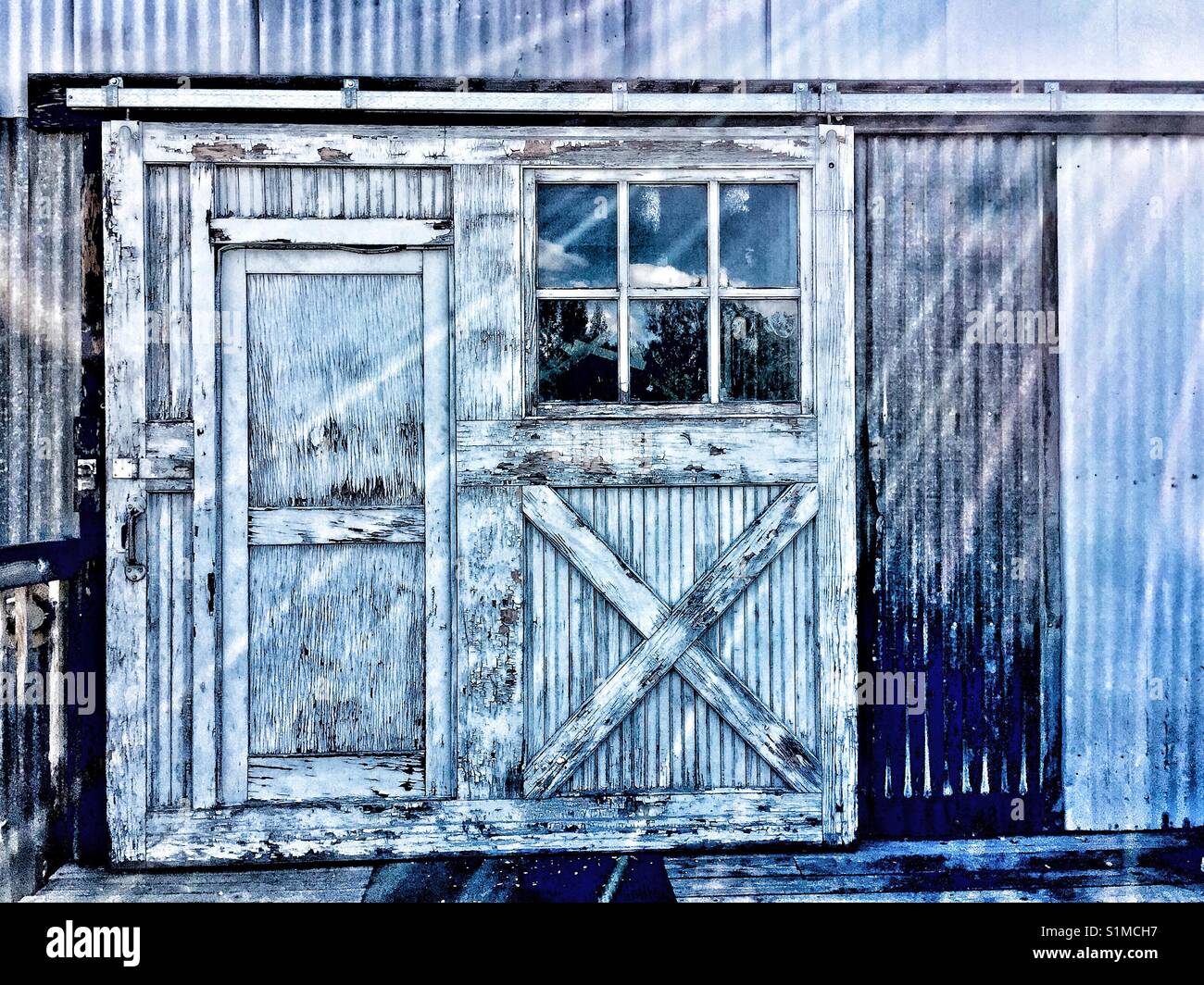 Close up of sliding barn door with window and entry on exterior wall of old corrugated iron industrial building. Stock Photo