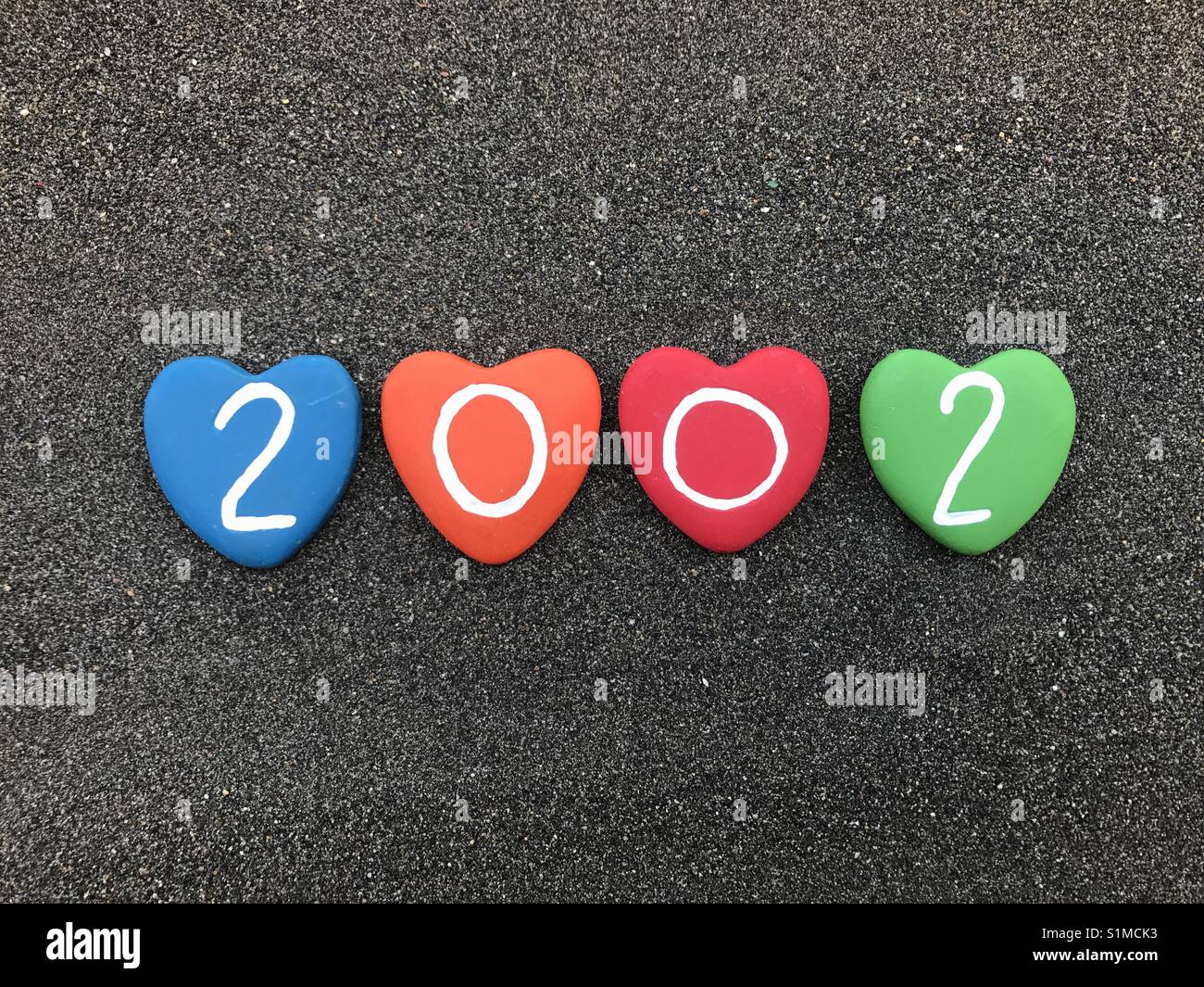2002 year with colored heart stones over black volcanic sand - Smartphone Captured Stock Image