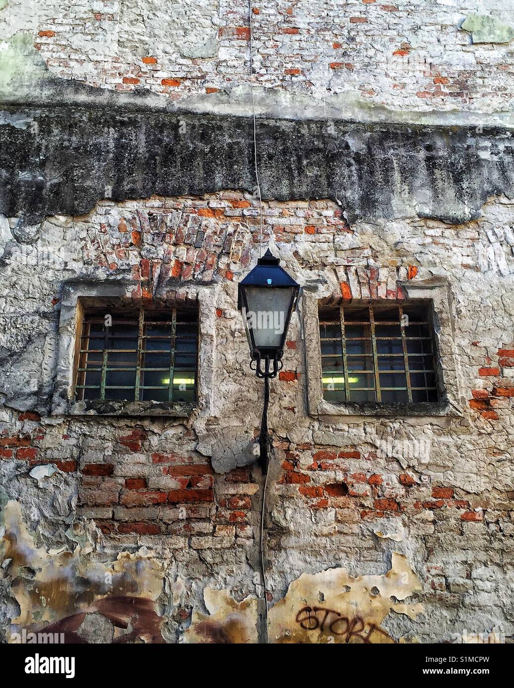 Brick wall of old derelict building with metal bars windows and street light out front. Croatia Stock Photo