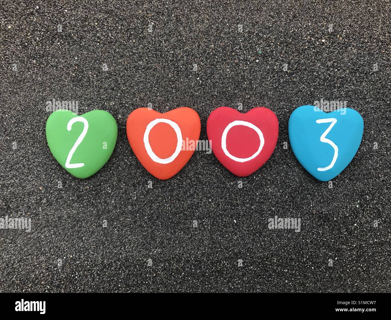 2003 year with colored heart stones over black volcanic sand - Smartphone Captured Stock Image