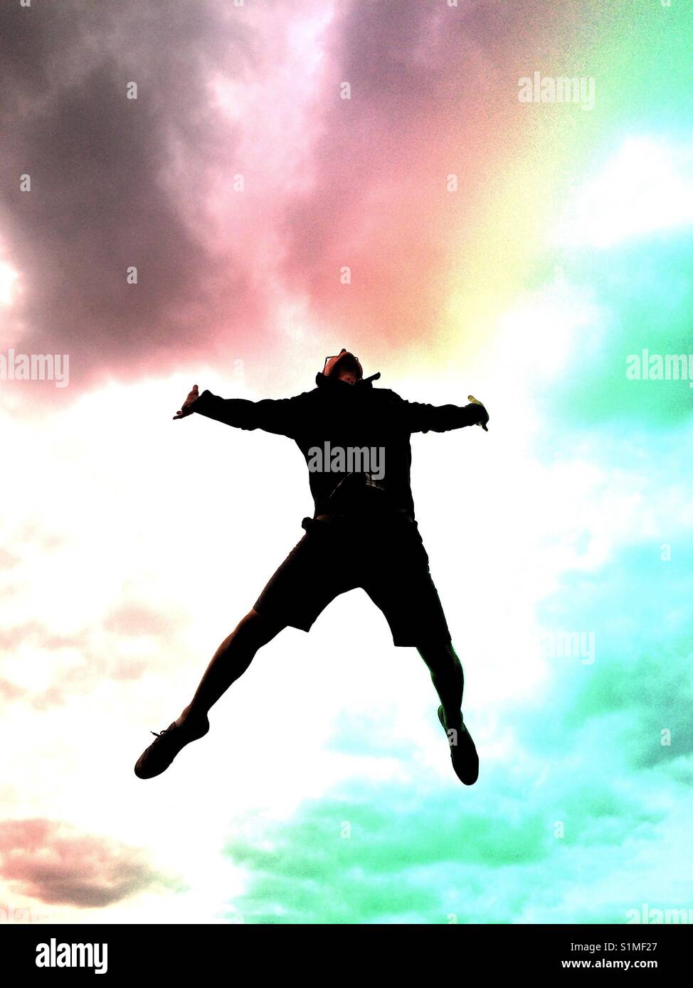A man jumping high in the air with his arms and legs spread as if falling with a dramatic, stormy sky behind - Smartphone Captured Stock Image
