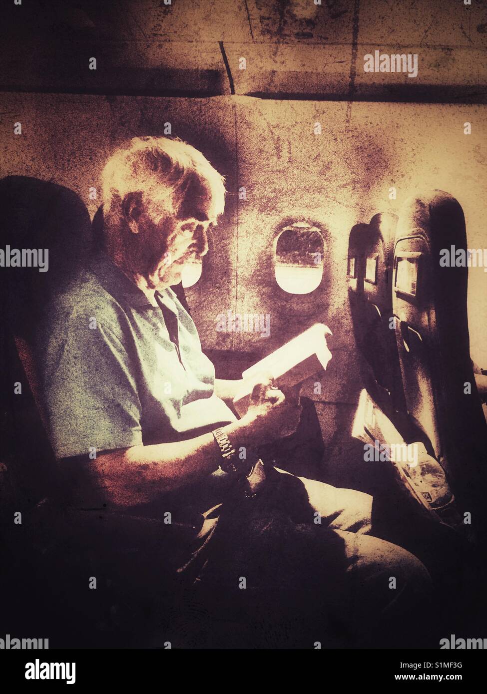 Senior man reading a book on an aeroplane at night, waiting for take-off - Smartphone Captured Stock Image