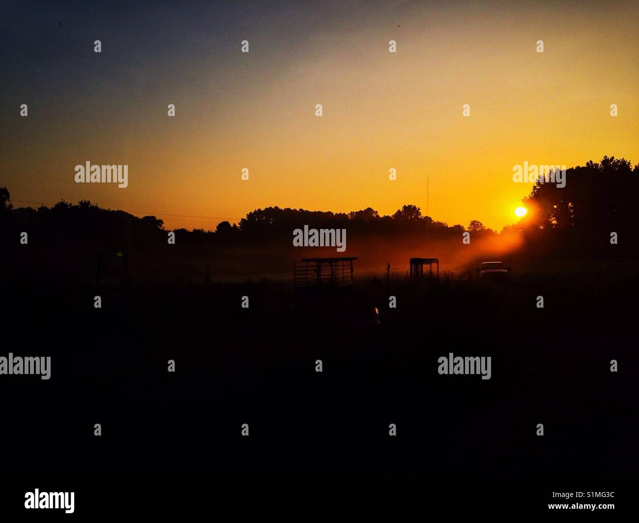 Machinery in the mist- sunrise through fog surround farm equipment, trees, and fields in rural North Carolina - Smartphone Captured Stock Image