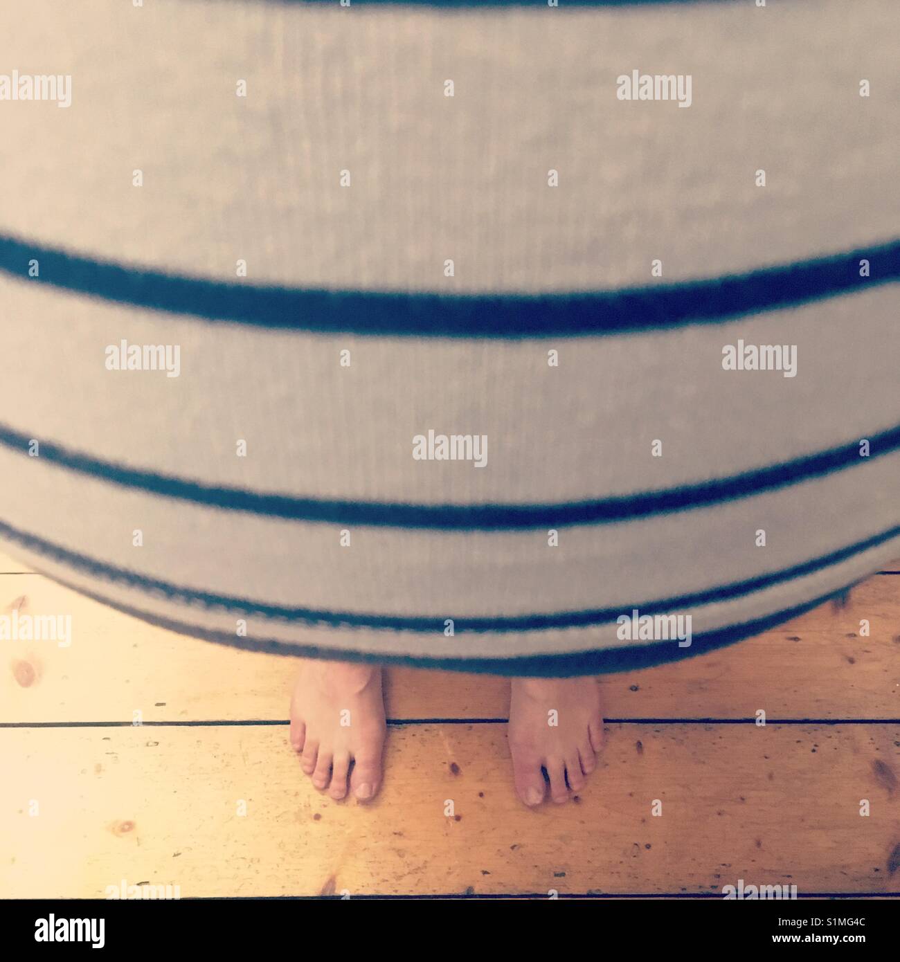 View of a pregnant woman's stomach from the top wearing a striped top on a wooden floor - Smartphone Captured Stock Image