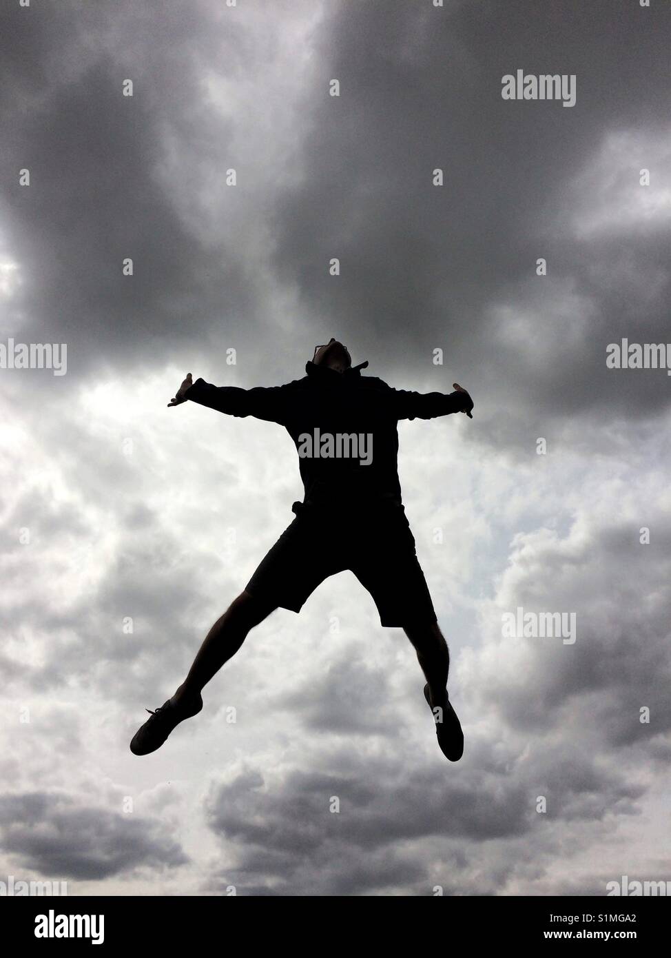 The silhouette of a man jumping or leaping high in the sky for joy and freedom with a dramatic sky behind Stock Photo