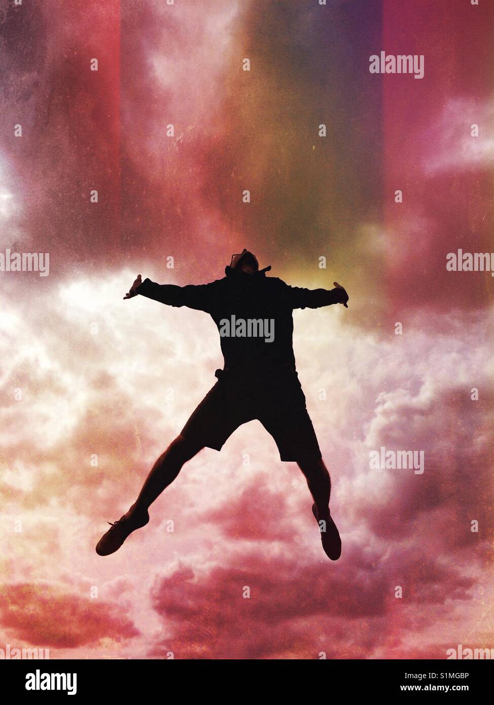 The silhouette of a man jumping high in the air with a stormy red sky and cloud behind. - Smartphone Captured Stock Image