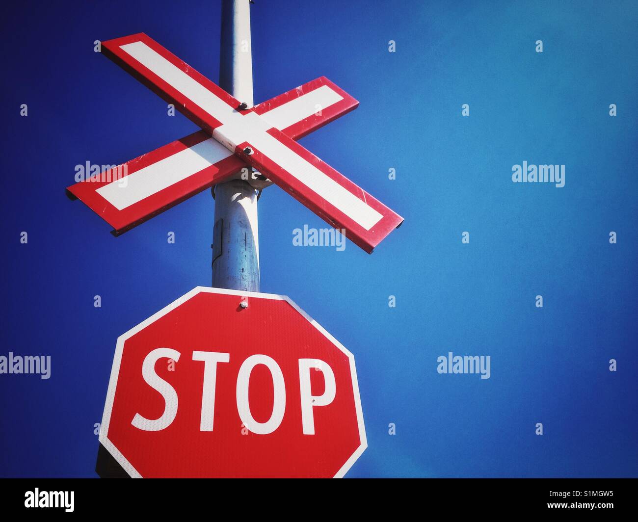 Stop sign and railway crossing signs against bright blue clear sky, North America. - Smartphone Captured Stock Image