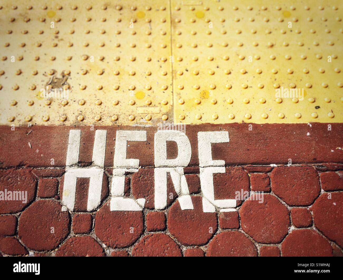 The word 'here' spelled out in white lettering over rust coloured paving bricks. Stock Photo