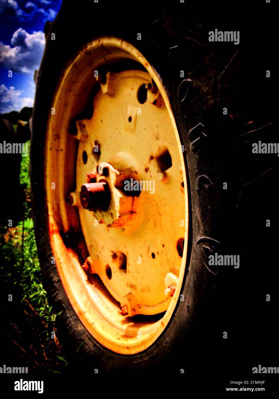Closeup of rear tractor tire and wheel in green field with blue sky - Smartphone Captured Stock Image