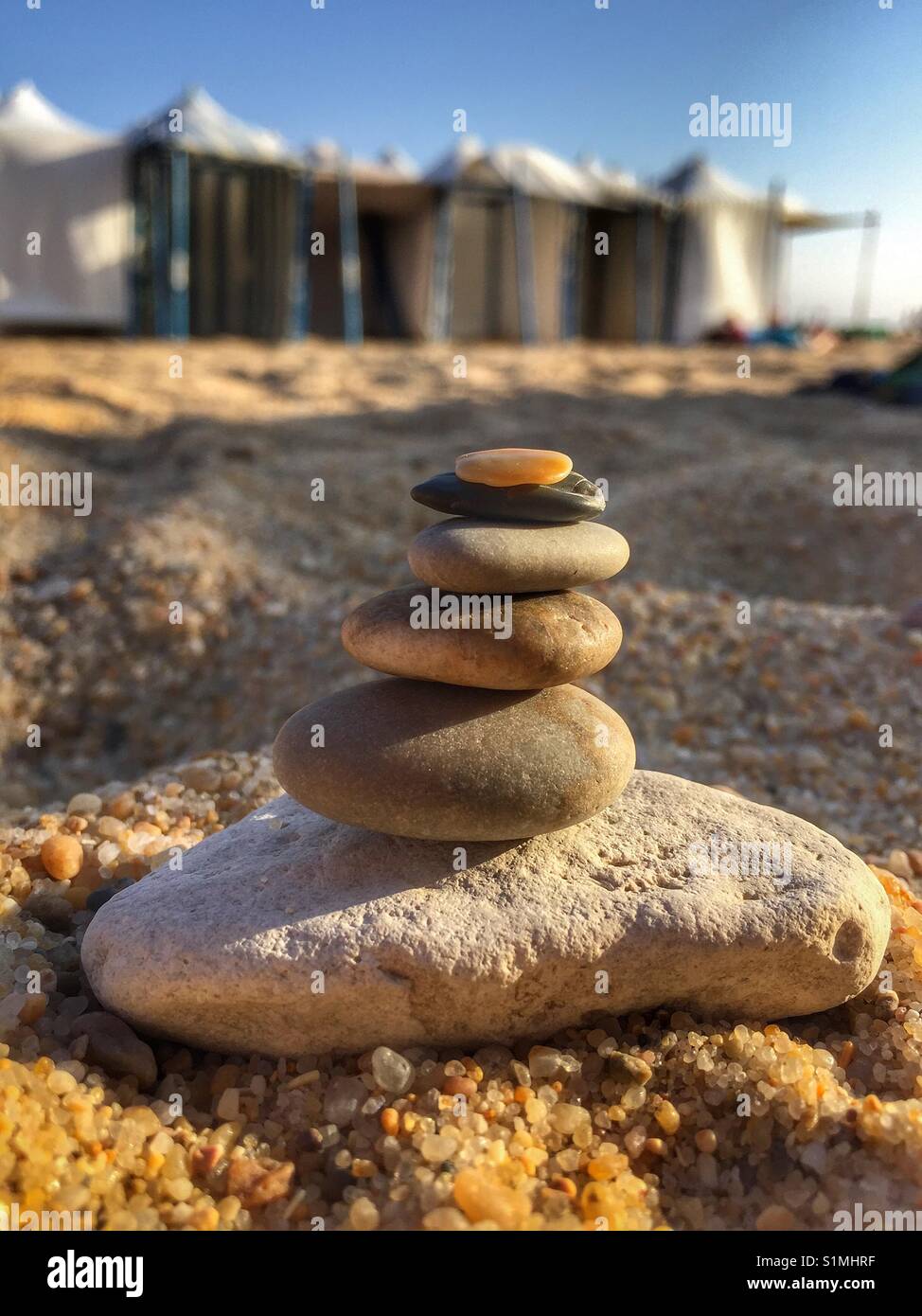 little stones stacked in the beach sand with barracs in the background - Smartphone Captured Stock Image