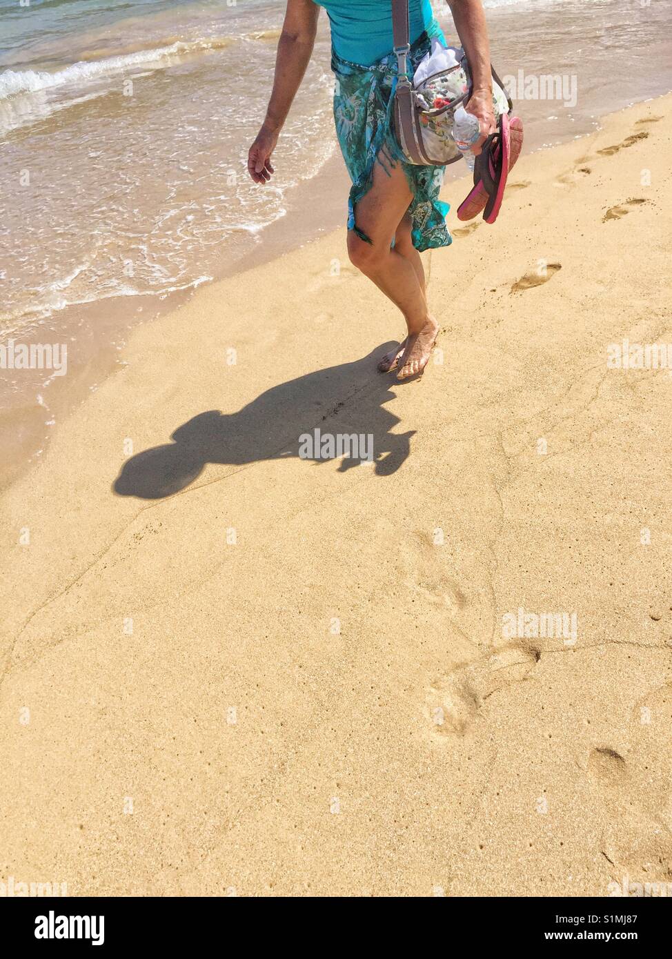 Woman walks along the waters edge on beach. Stock Photo