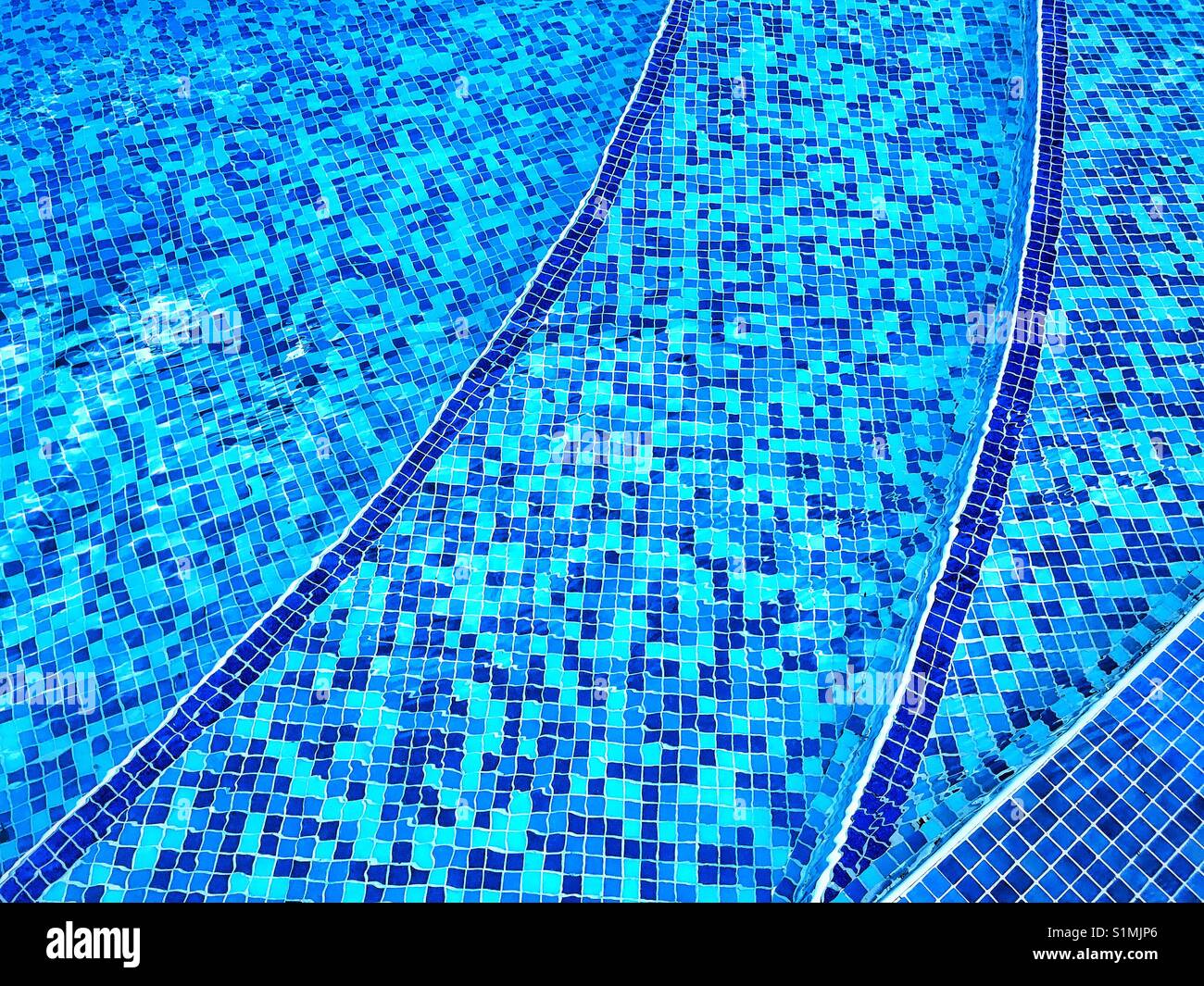 Small blue tiles make up the bottom of the steps into a large swimming pool. The water is clear, the sun is shining - it's time to go swimming! Photo Credit - © COLIN HOSKINS. - Smartphone Captured Stock Image