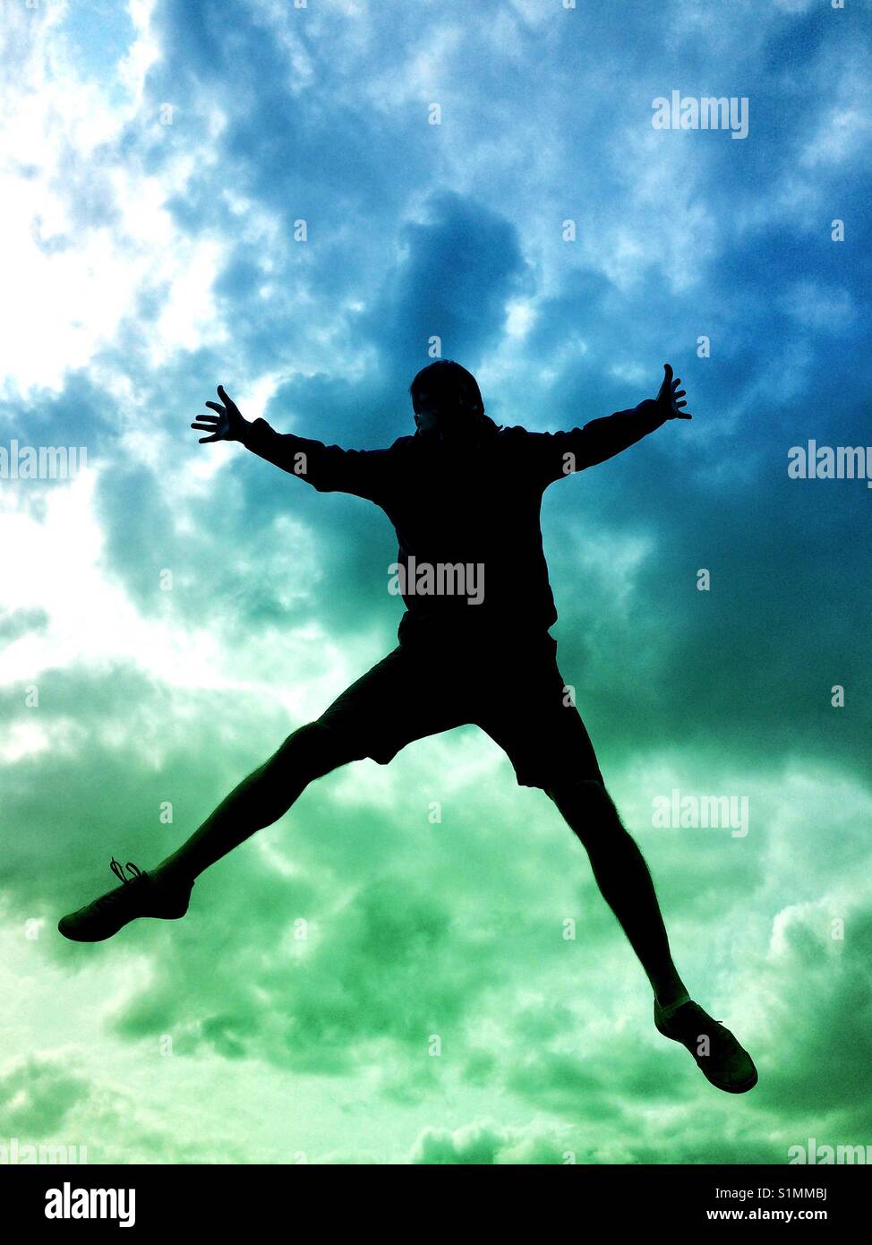 The silhouette of a man jumping high in the air or falling from the sky with a colourful, stormy sky behind. - Smartphone Captured Stock Image