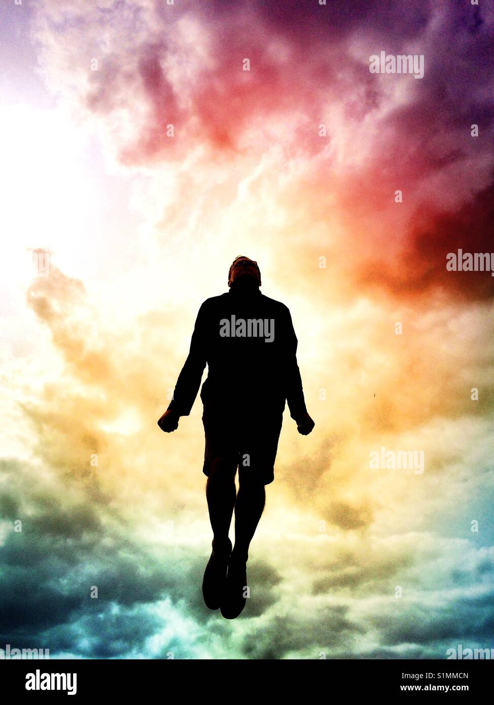 The figure or silhouette of a man floating or jumping high in the sky with a colourful, stormy sky behind. Stock Photo