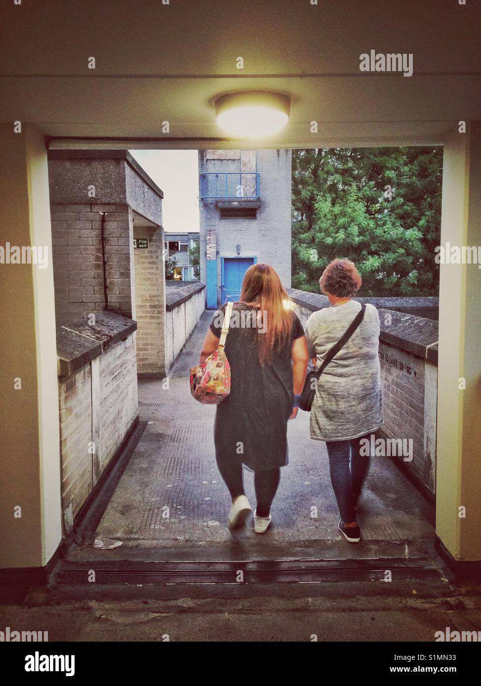 A couple of women walk along a concrete walkway in the early evening. - Smartphone Captured Stock Image