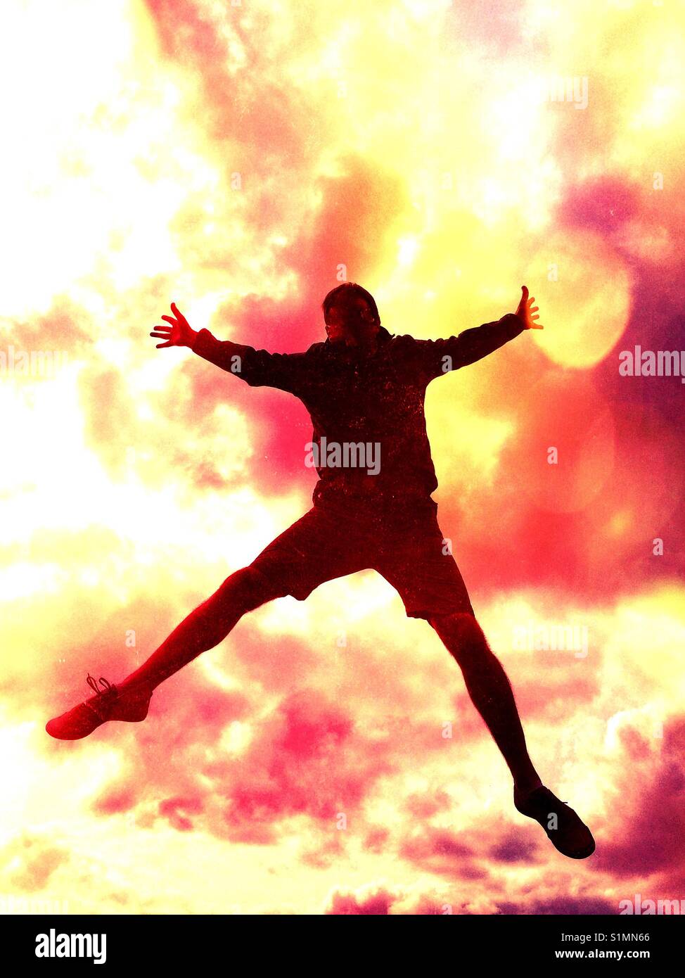The silhouette of a man falling or jumping high in the air with a dramatic explosion in the background. - Smartphone Captured Stock Image