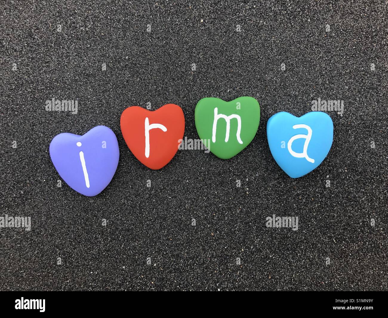 Irma, feminine name with colored heart stones over black volcanic sand - Smartphone Captured Stock Image