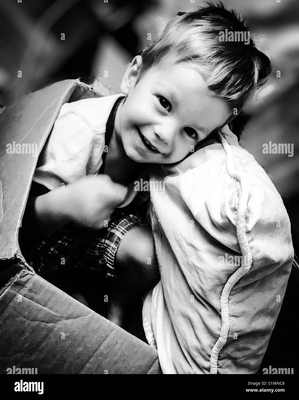 Smiling toddler sitting ina cardboard box along with his favorite pillow. Stock Photo