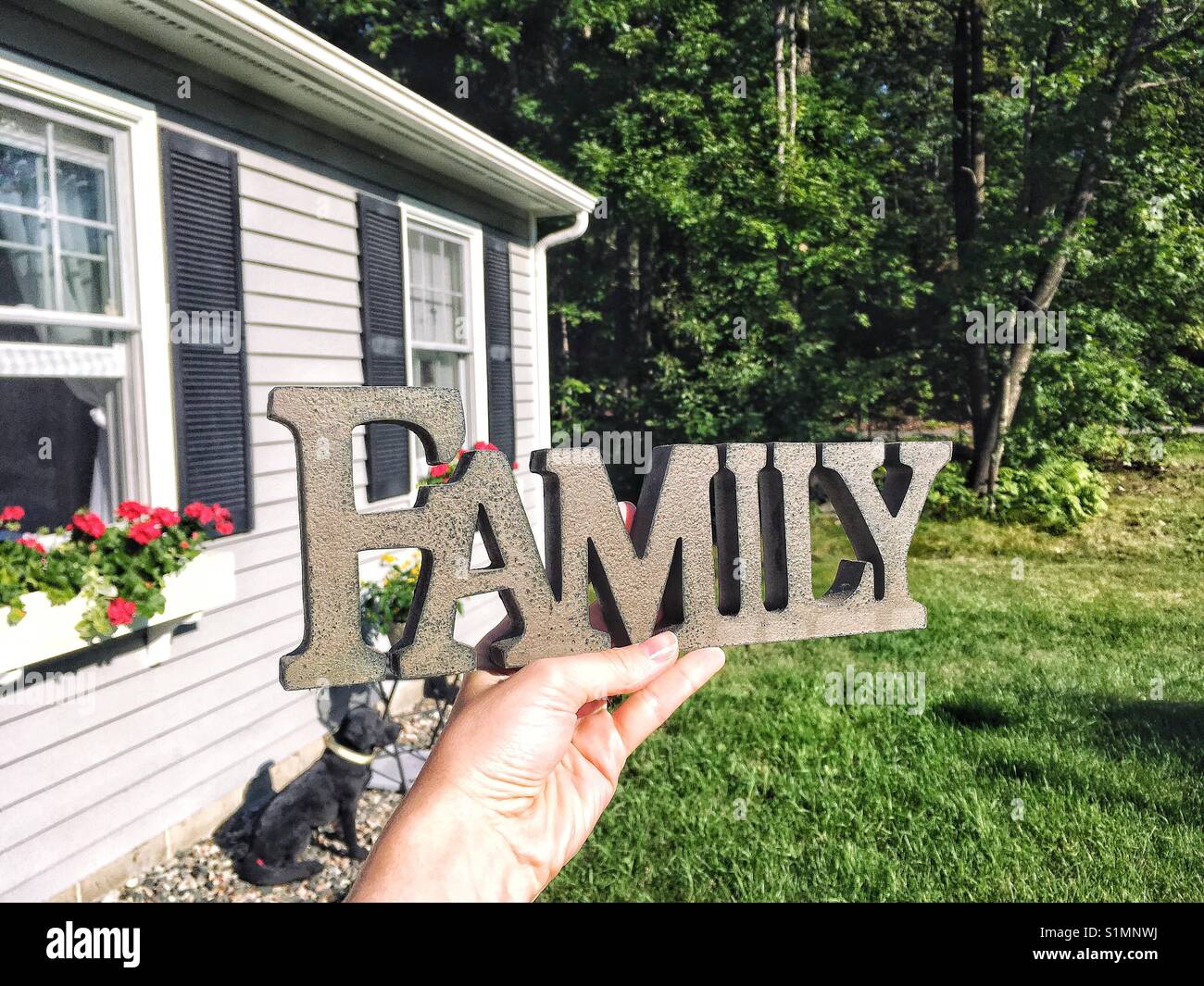 Family wooden sign in a hand against house - Smartphone Captured Stock Image
