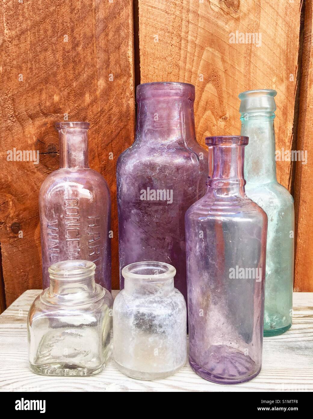 A collection of vintage and antique blown glass and machine made bottles on wood table with wood fence background. Includes ink, medicine, and condiment bottles. Stock Photo