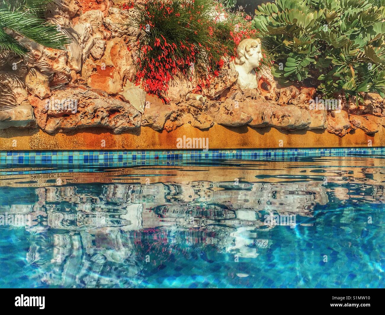 Sparkling water of a blue tiled swimming pool with an integral rockery and Roman bust feature. - Smartphone Captured Stock Image
