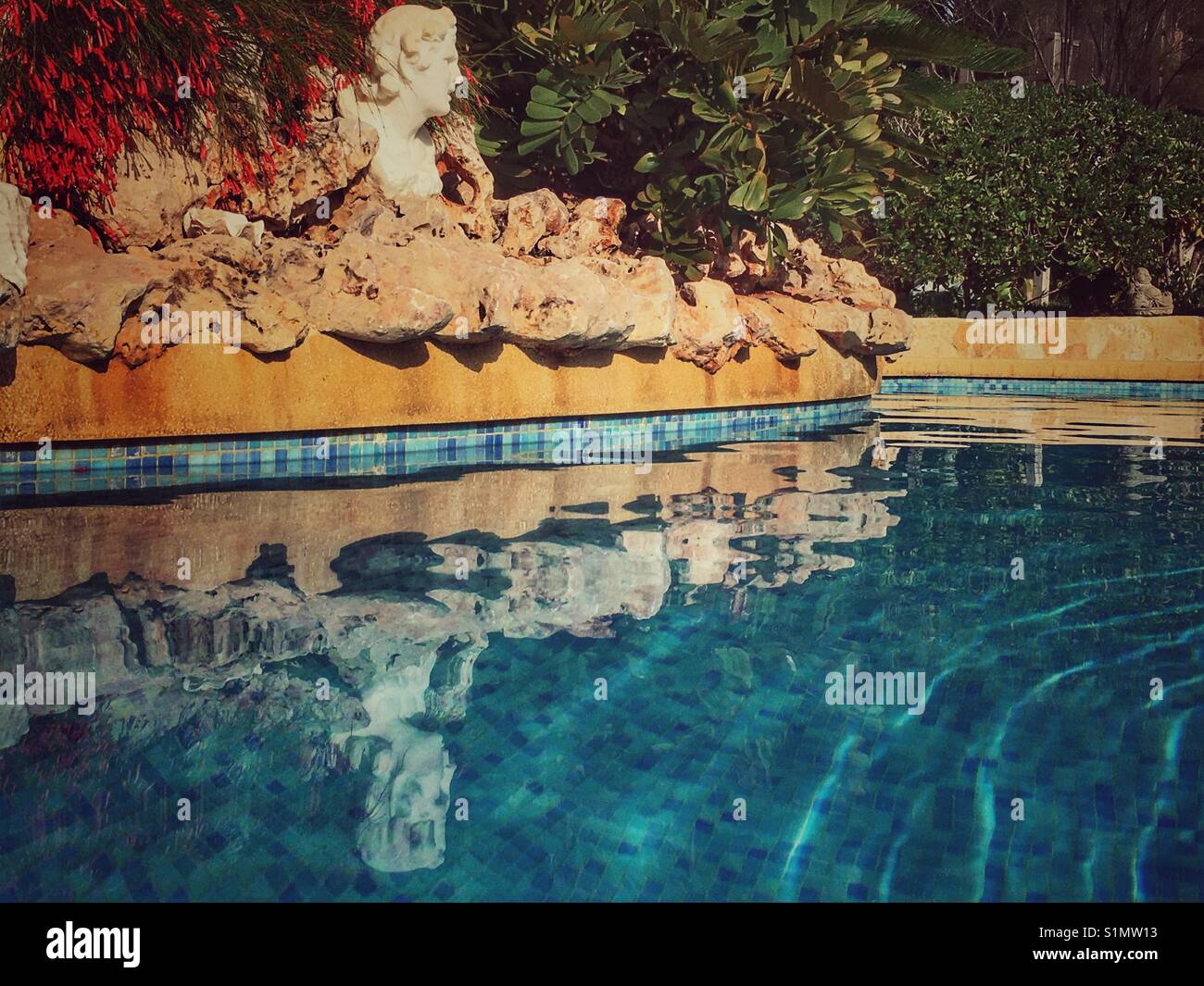 Sparkling water of a blue tiled swimming pool with an integral rockery and Roman bust feature. - Smartphone Captured Stock Image