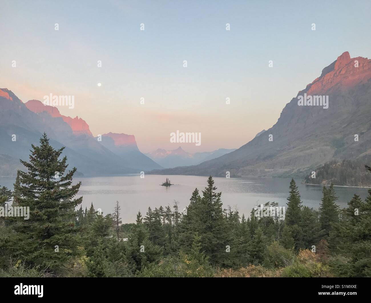 Goose Island in St Mary Lake, Glacier National Park. Taken at sunrise with wildfire smoke causing a haze in the distance. - Smartphone Captured Stock Image