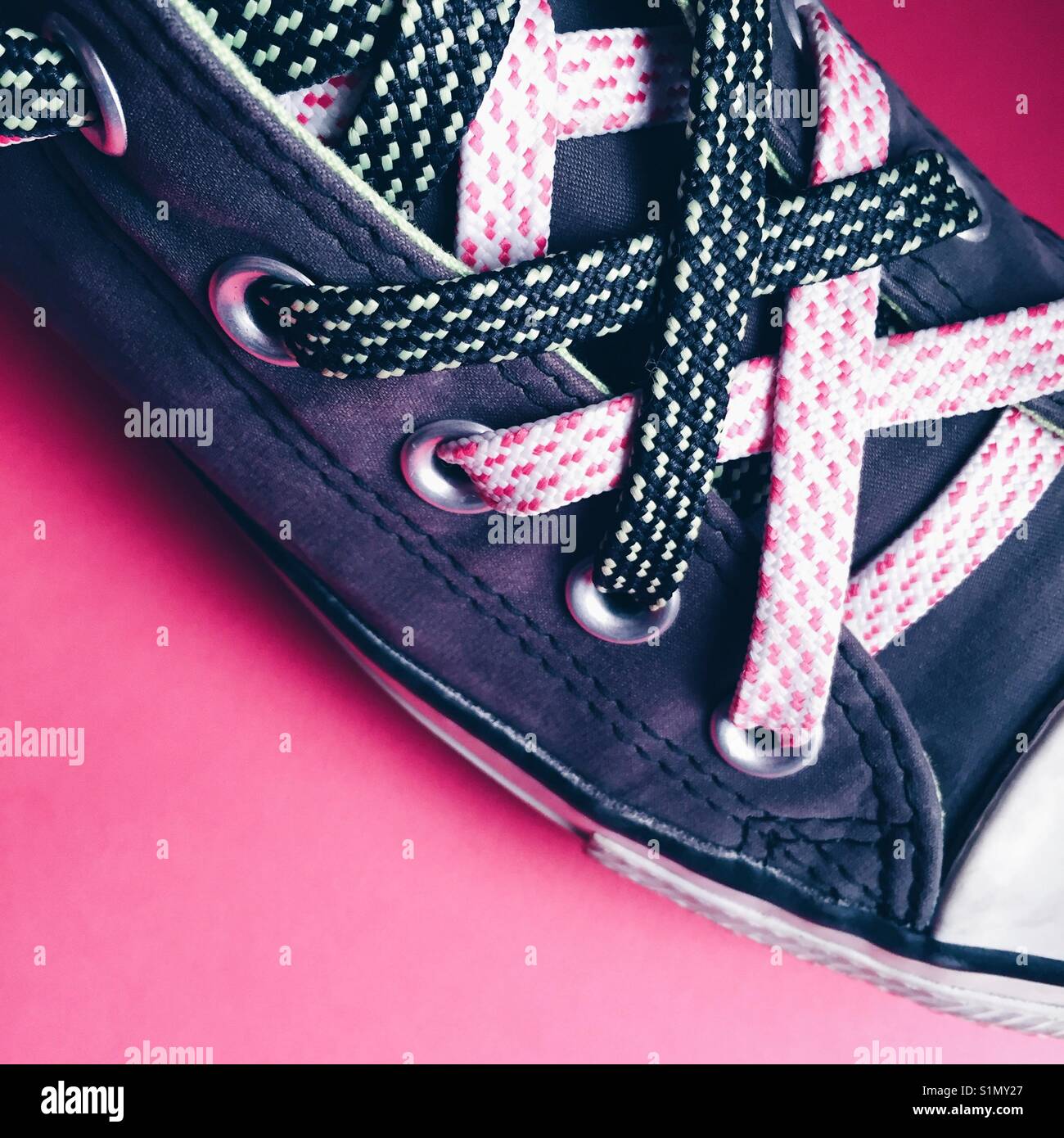 a close up detail shot of a womans sneaker with funky laces on a pink S1MY27