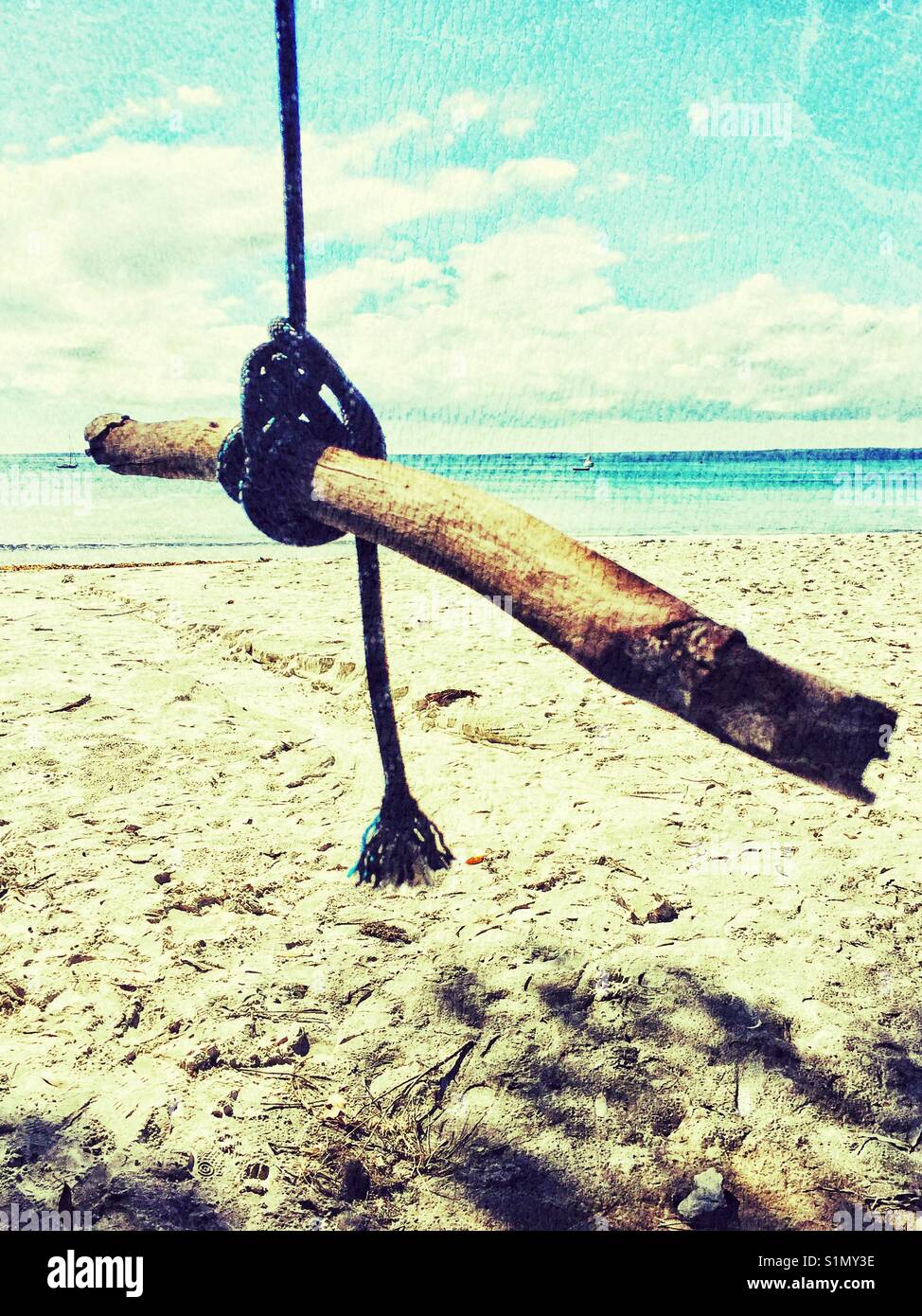 Empty beach swing on seashore. Swing made from a tree branch and rope on beach. Stock Photo