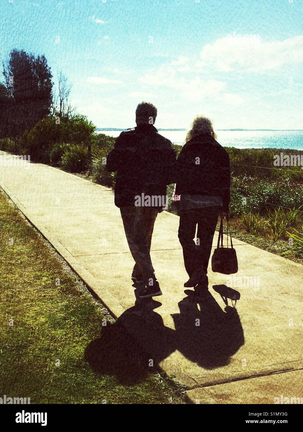 Couple walking down footpath beside the waterfront. Vincentia, NSW, Australia Stock Photo
