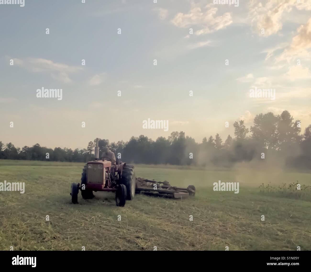 Tractor approaches pulling mower and leaving cloud of dust under North Carolina evening sky - Smartphone Captured Stock Image
