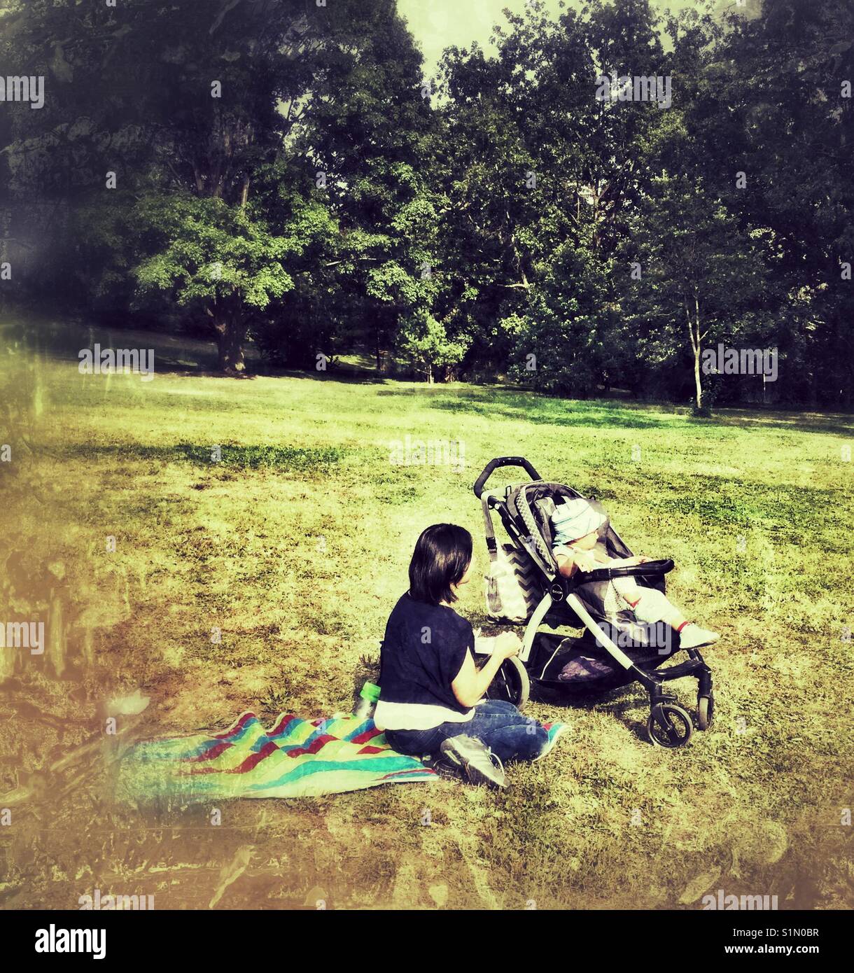 Mother and daughter sit on grass in a park. - Smartphone Captured Stock Image