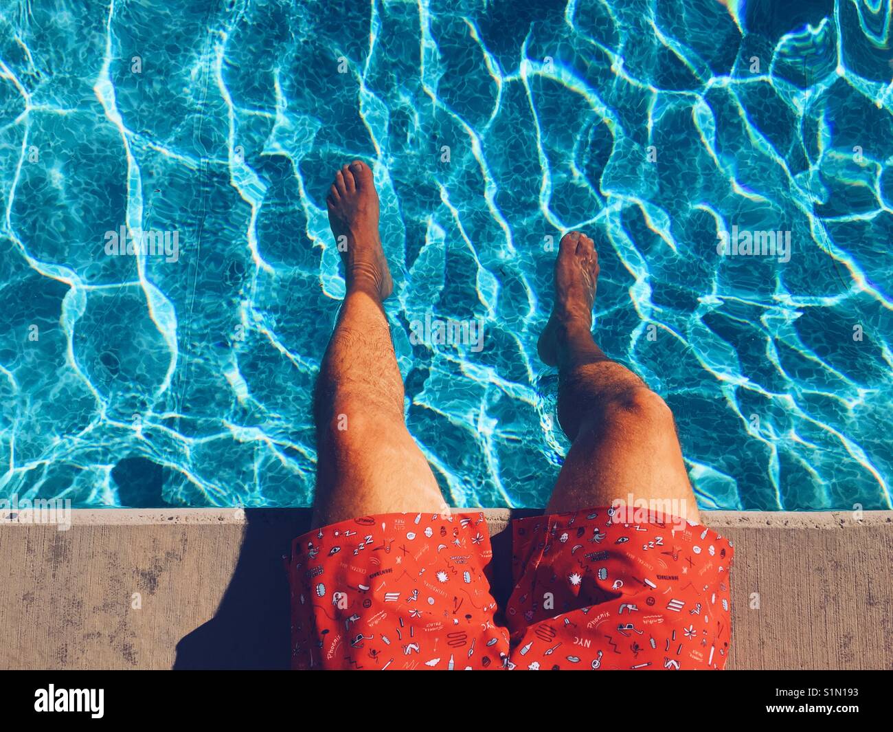 Areal view of the legs of man sitting at the edge of a swimming pool on a sunny hot day. - Smartphone Captured Stock Image